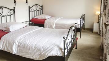 A room with two single beds, each with a white mattress and red bedding. There are wall-mounted light fixtures above the beds.