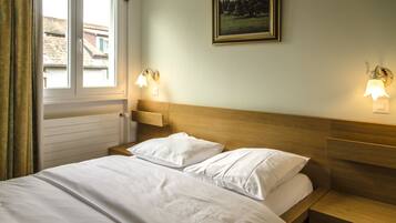 A hotel room with a wooden headboard, two bedside tables, a bed with white linens, two wall-mounted lamps, and a framed picture on the wall.