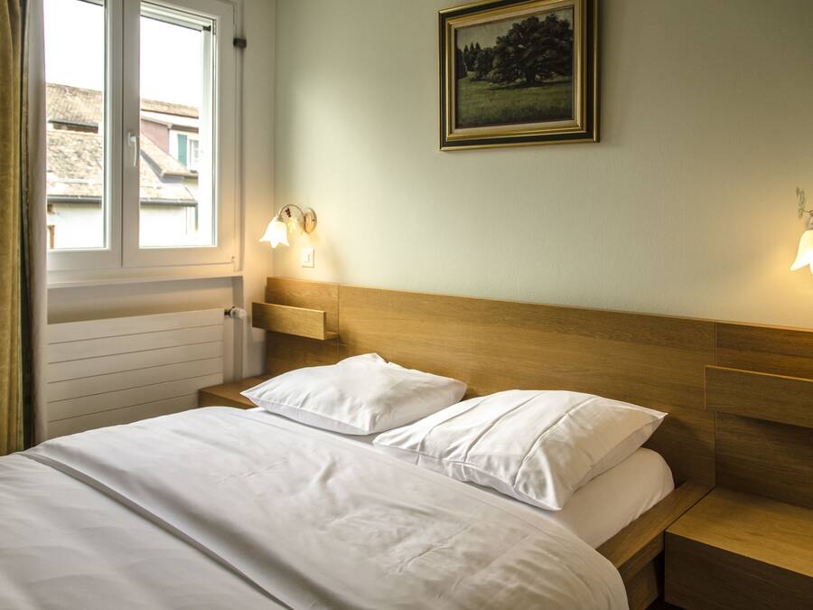 A hotel room with a wooden headboard, two bedside tables, a bed with white linens, two wall-mounted lamps, and a framed picture on the wall.