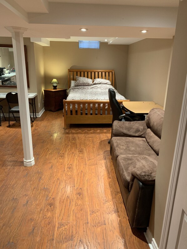 A compact bedroom with a bed, a desk, a chair, and a sofa.