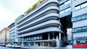 Un edificio moderno de varios pisos con fachada curva, ventanas grandes y una entrada visible con un letrero.