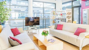 Una sala de estar moderna con un televisor de pantalla plana grande, dos sofás con cojines rojos, una mesa de centro con un florero y una estantería.