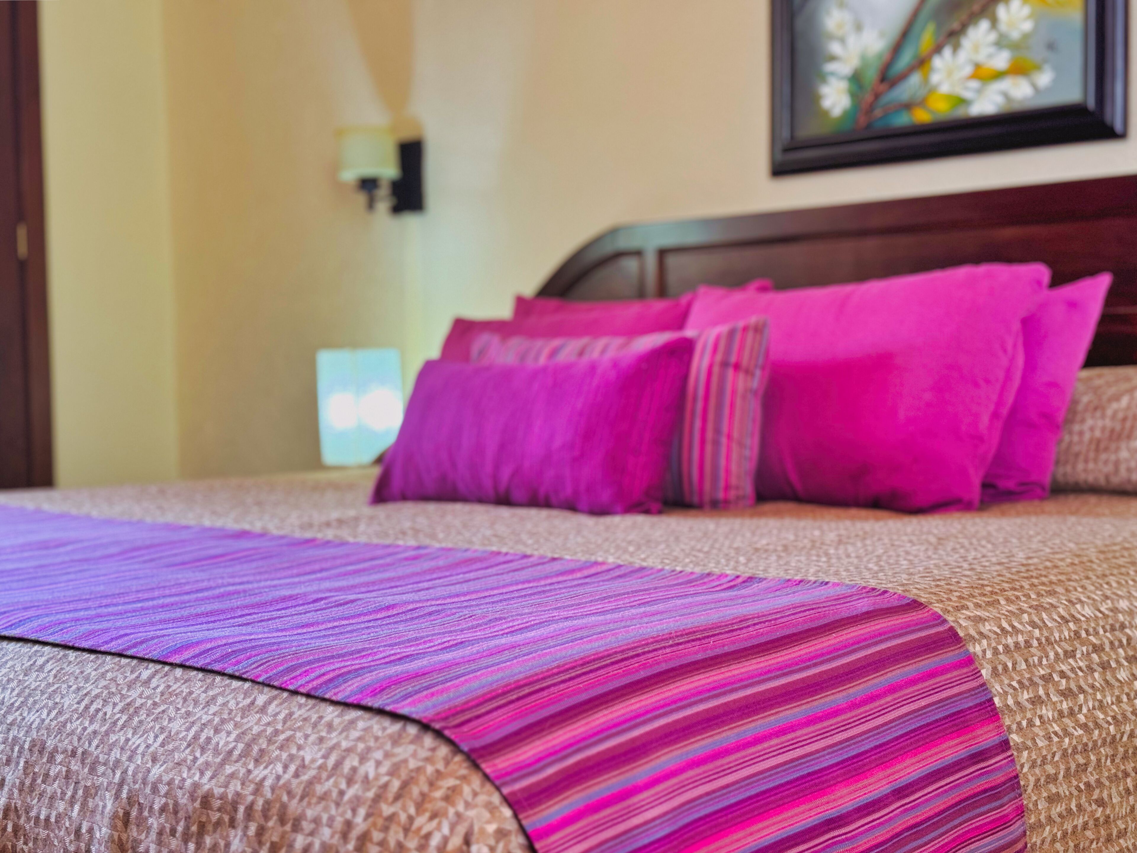 A bed with a purple and pink striped blanket, a wooden headboard, and pink pillows.