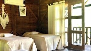 Una habitación rústica de madera con dos camas, un adorno de macramé colgado y un cuadro en la pared.