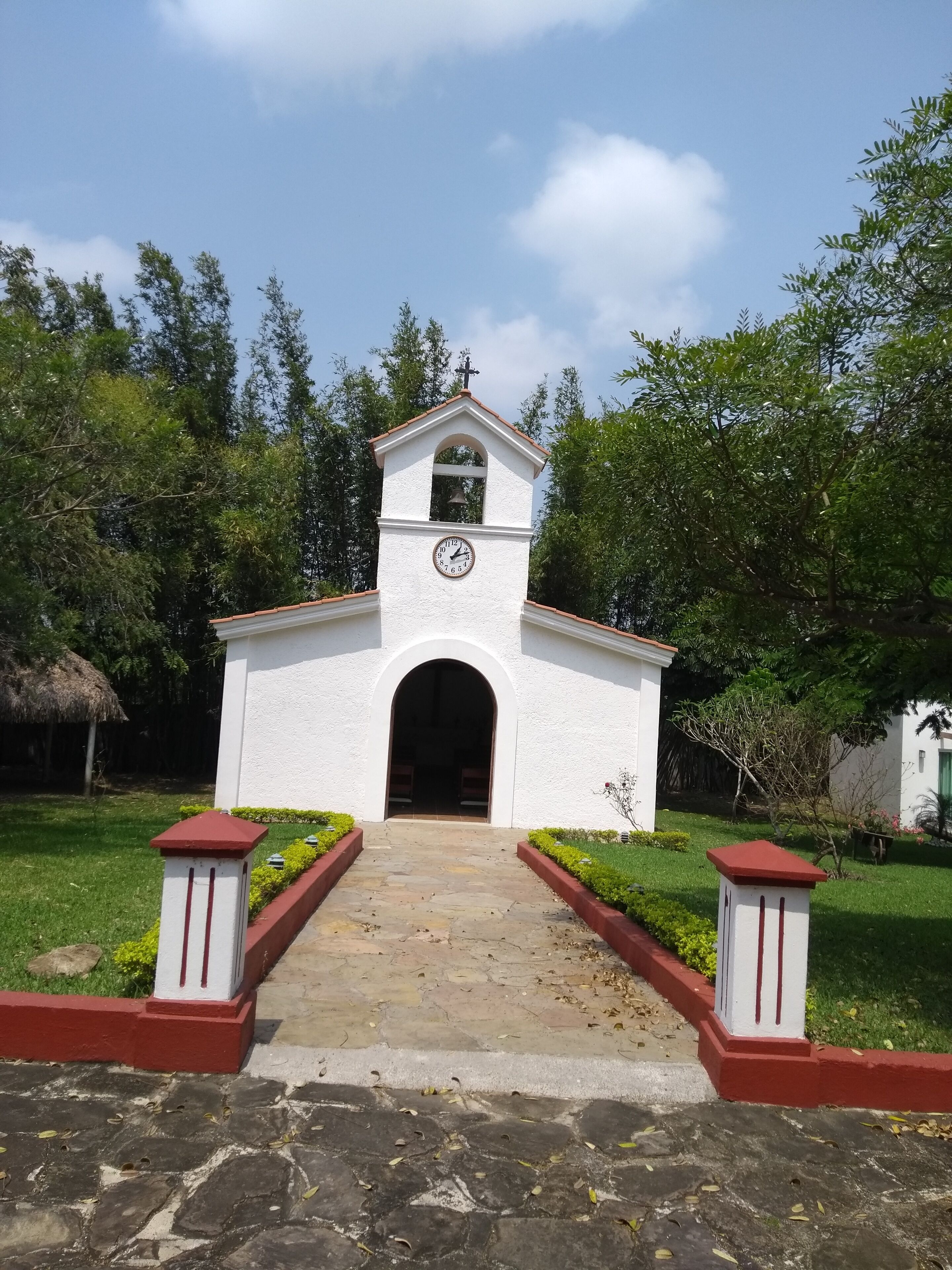 Una iglesia blanca con un reloj, una campana y una cruz en la parte superior.