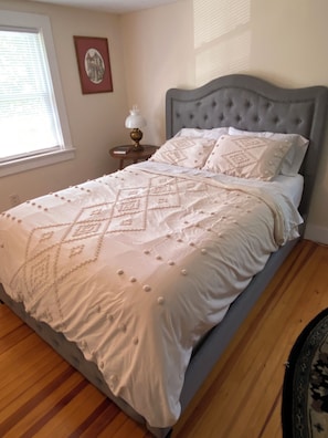 Una cama bien hecha con colcha y almohadas estampadas, una lámpara de noche y un cuadro en la pared.