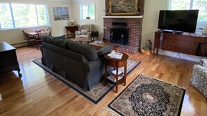 A living room with a fireplace, a sofa, a television, and a dining area. - Quintessential Cape Vibes in Boothbay (Boothbay)