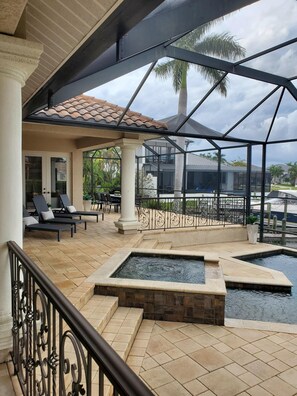 A covered outdoor area with a pool, lounge chairs, and a view of a residential building. - Luxury Pool Spa Home with Spectacular Water View! (Cape Coral)