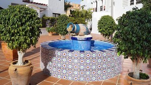 Ein Innenhof mit einem gefliesten Brunnen, Topfpflanzen und weißen Gebäuden mit Bögen.