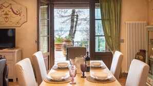 Ein Esszimmer mit einem Tisch für sechs Personen, einem Fernseher links und Blick auf Bäume und ein Gewässer durch die geöffnete Tür.