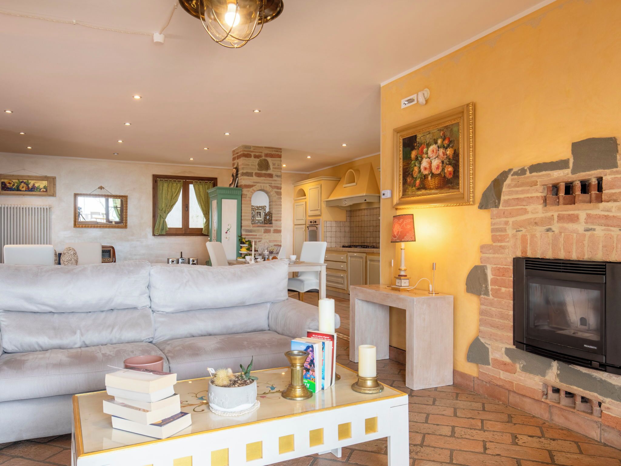 Una sala de estar con un sofá, una mesa de centro con libros y una planta, una chimenea y una cocina al fondo.