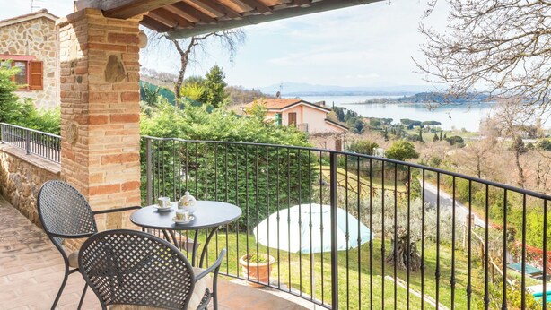 Ein Balkon mit Blick auf einen See, Steinbauten und einem Tisch mit Stühlen.