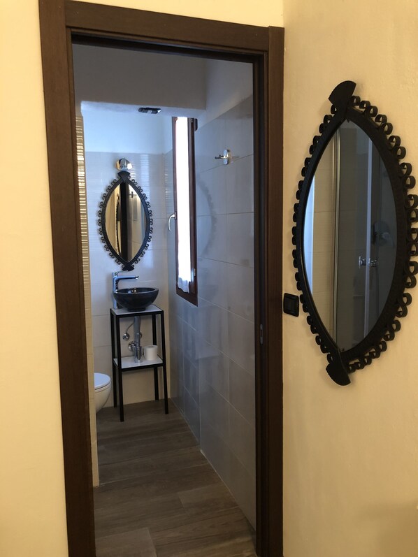 Pasillo que lleva a un baño con inodoro, lavabo y espejo con marco decorativo.
