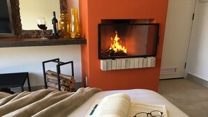 A cozy room with a fireplace, a bed with a book and glasses, and a shelf with bottles and a vase. - Latitude Lodge (Cunha)