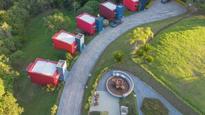 An aerial view of a residential area with multiple red and blue buildings, a winding driveway, and a circular outdoor seating area with a fire pit. - Latitude Lodge (Cunha)