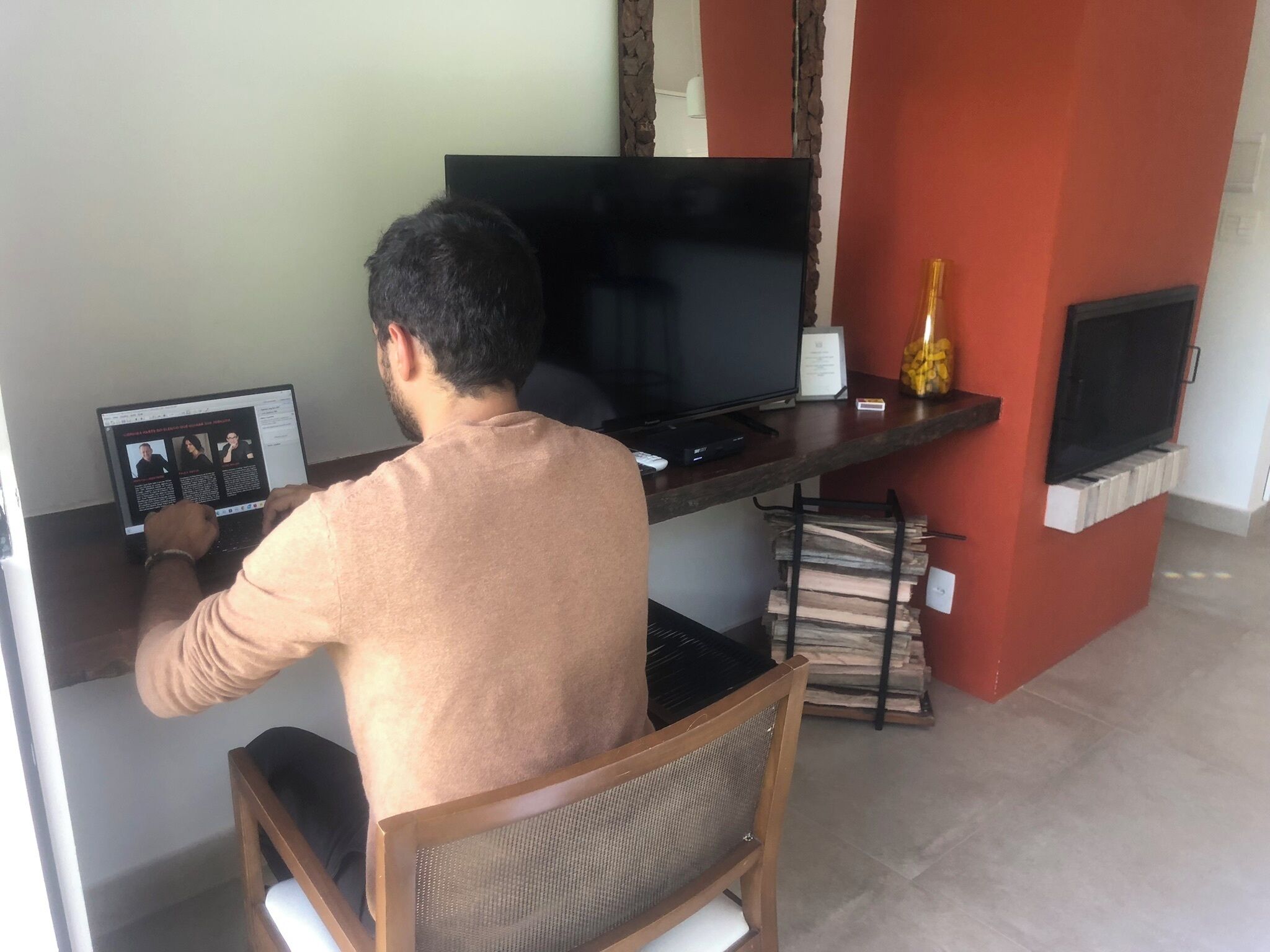 A person sitting at a desk with a laptop and a television.