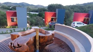 A modern building with a unique wooden sculpture centerpiece, surrounded by red and blue structures, set against a hilly backdrop. - Latitude Lodge (Cunha)