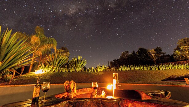 A night scene with a starry sky, a wooden bench, a bottle, and a glass of wine. - Latitude Lodge (Cunha)