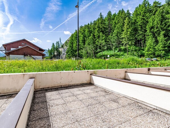 A paved area with a concrete bench, a building with a sloped roof, and a dense forest in the background. - Les Olympiques (Tignes 1800) by Interhome (Tignes)