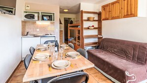 Um espaço compacto com cozinha compacta, mesa de jantar para quatro pessoas e um sofá marrom.