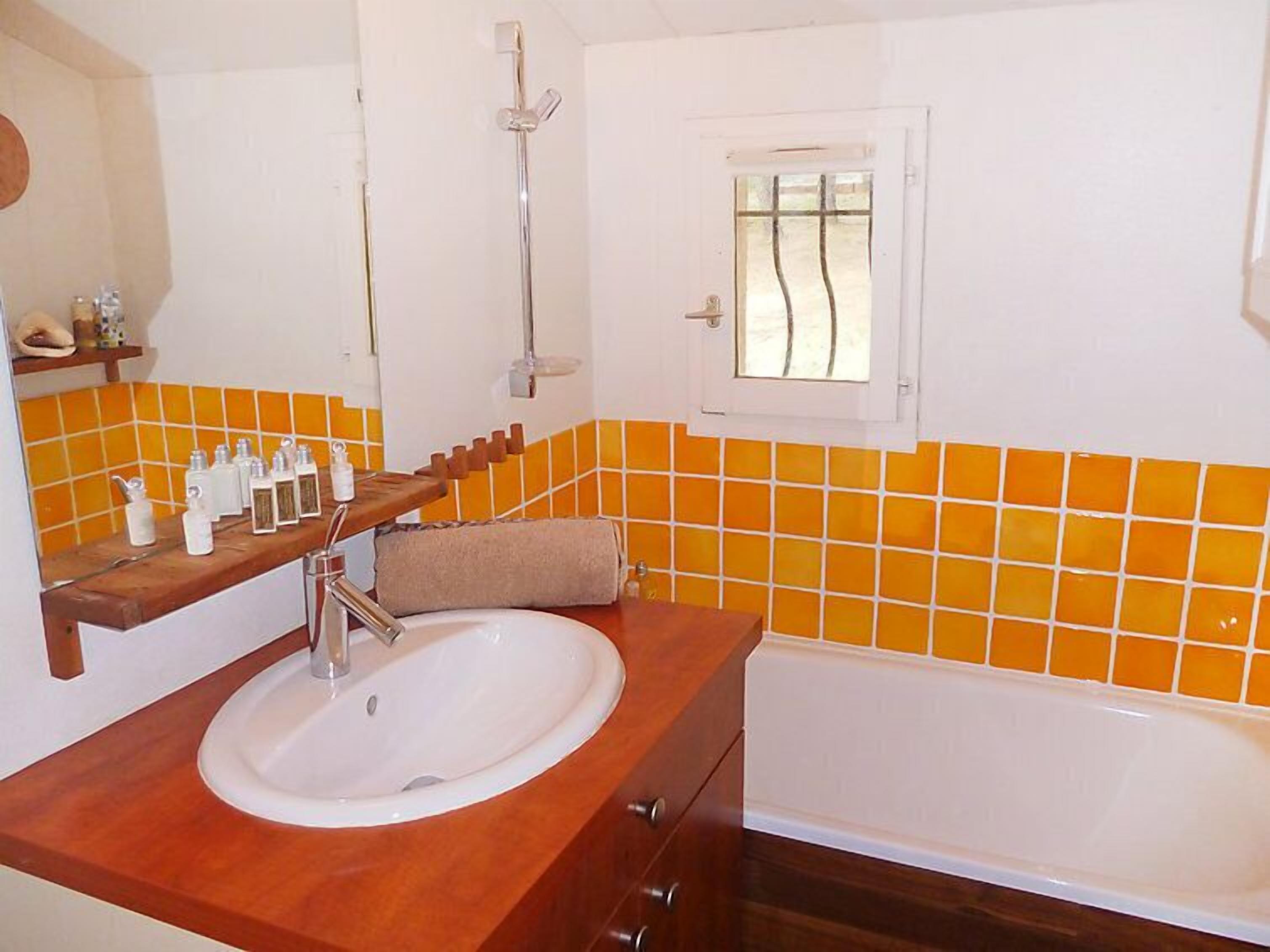 A bathroom with a wooden vanity, a white sink, a bathtub, and orange-tiled walls.