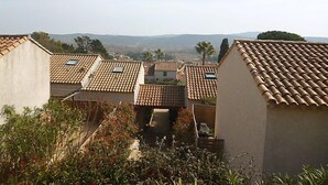 Un quartier résidentiel aux toits recouverts de tuiles en terre cuite, sous un ciel dégagé, avec des collines qui se dessinent à l’horizon.