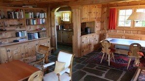 Ein gemütliches Blockhaus-Interieur mit Holzwänden, Steinböden, einem Esstisch mit Stühlen, einer Küchenzeile und einem Bücherregal.