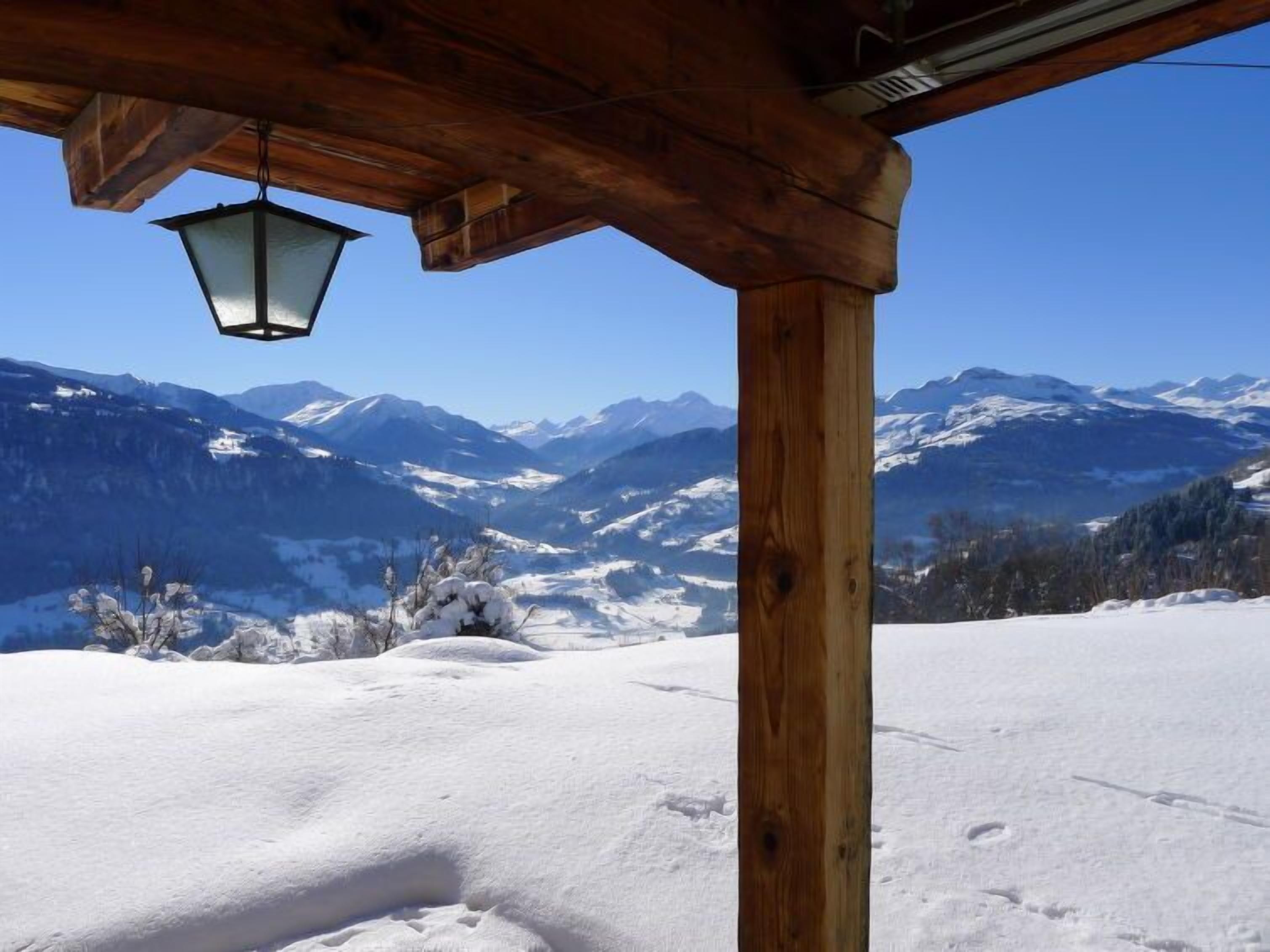 Une structure en bois sur laquelle est suspendue une lanterne, offrant une vue sur un paysage montagneux enneigé.