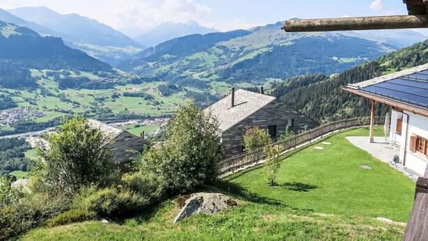 Blick auf Berge mit einem Haus, das ein Solardach, einen umzäunten Garten und einen Kiesweg hat.