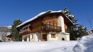 Ein Chalet-Stil Gebäude mit Holzfassade und Balkon, umgeben von schneebedeckten Bäumen und blauem Himmel.