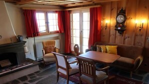 Ein gemütlicher Raum mit Steinboden, Kamin, einem Holzespeisetisch mit Stühlen, einer Couch mit Kissen und einer Wanduhr.