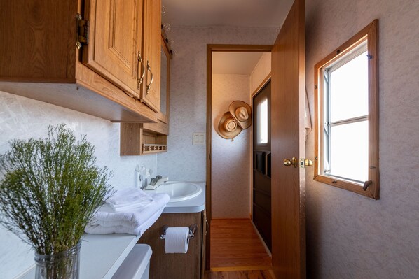 A compact bathroom with wooden cabinets, a white sink, and a window providing natural light. - Soul of the Desert (Alpine)