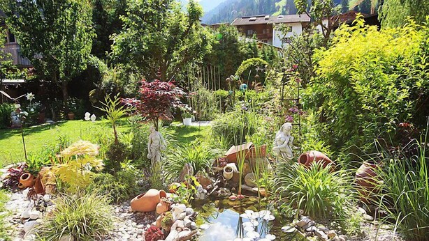 Een tuin met een vijver, diverse planten en een beeld.