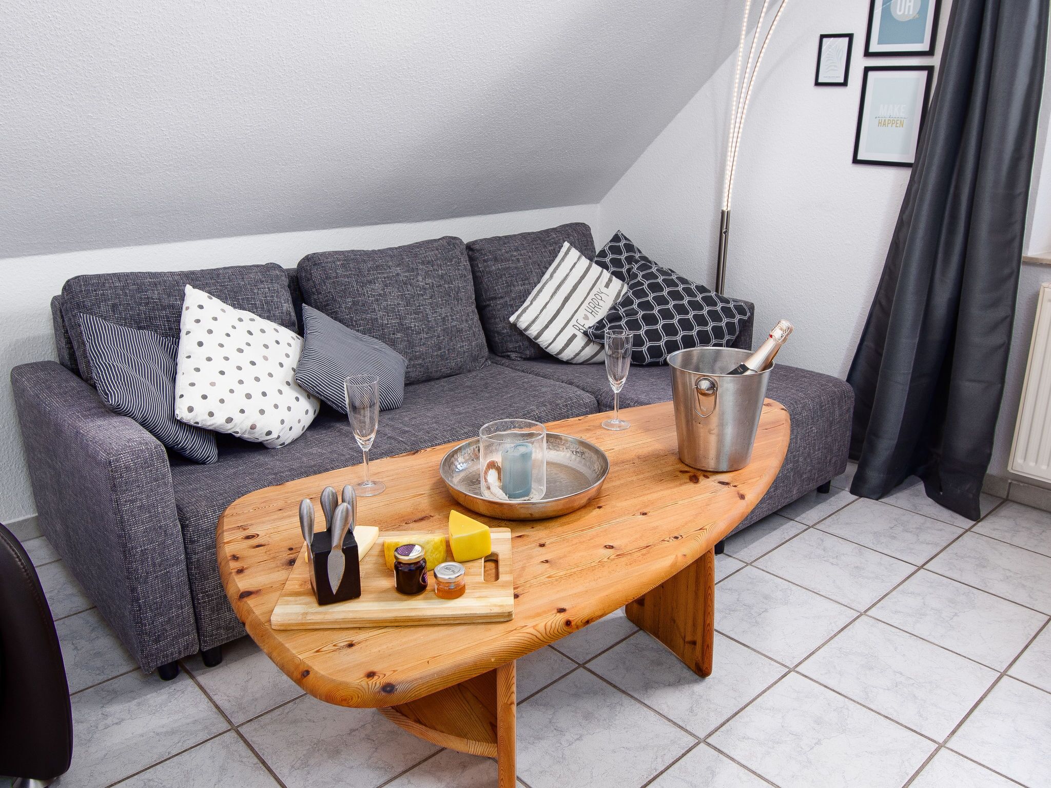 Ein modernes Wohnzimmer mit einem grauen Sofa, einem Holztisch mit Lebensmitteln, einem Metallkübel mit einer Flasche und einem Glas.
