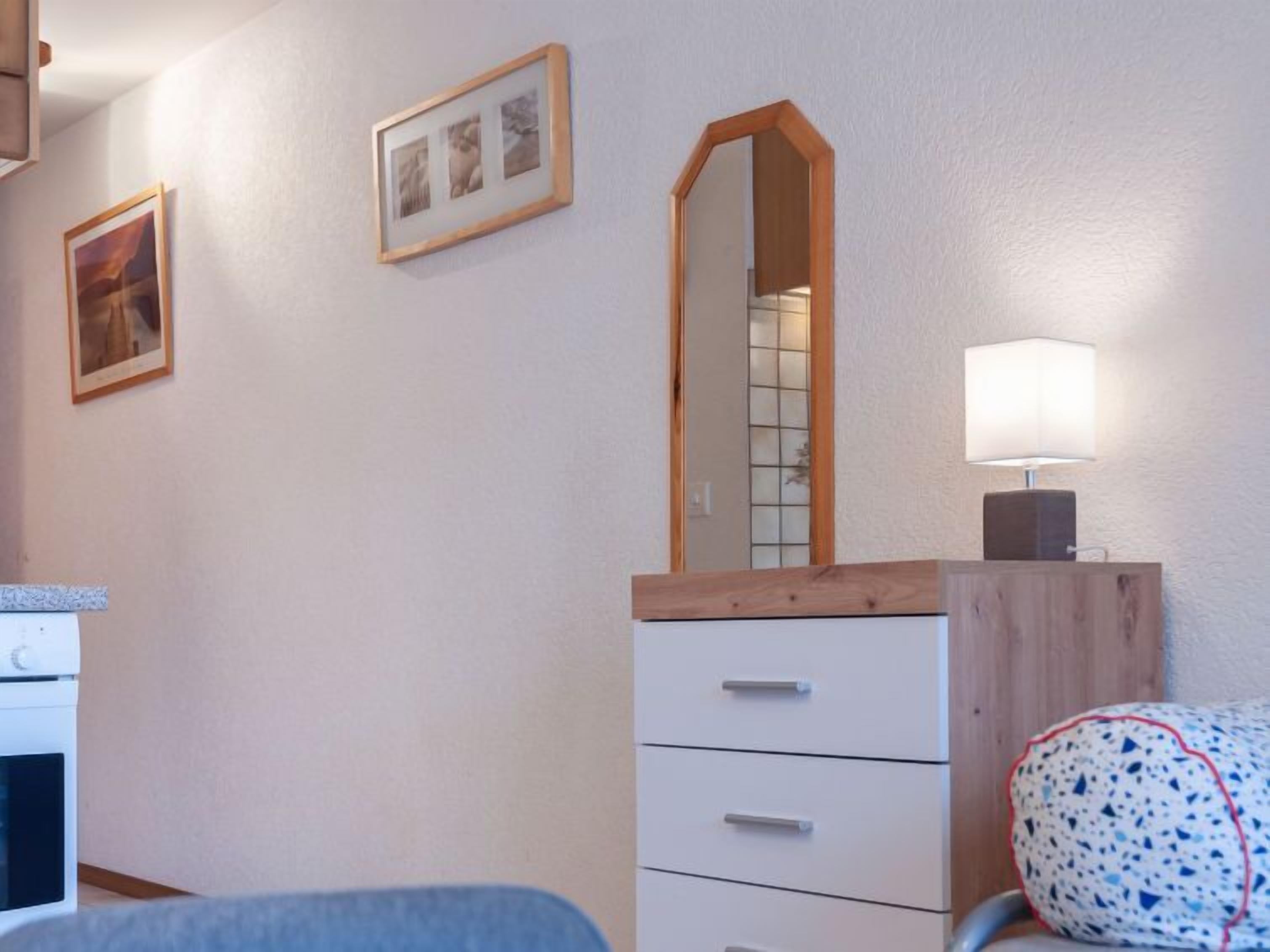 Een slaapkamer met een bed, een dressoir met lades, een spiegel en een wandlamp.