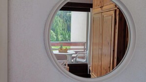 A room with a circular window revealing a balcony with a table and chairs, and a wooden cabinet. - Rosablanche B72 by Interhome (Siviez-Nendaz)