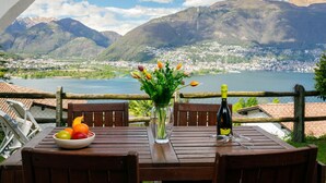 Une table ornée d’un saladier de fruits, d’un vase de fleurs et d’une bouteille de vin, le tout placé devant un paysage montagneux pittoresque.