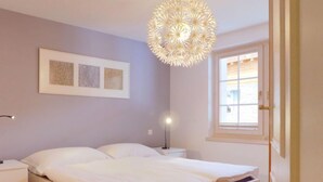 Een slaapkamer met een bed, nachtkastjes, een wandlamp, een raam en kunstwerken in lijsten.
