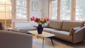 Een moderne woonkamer met een bank, fauteuil en salontafel. Op de tafel staat een vaas met bloemen.