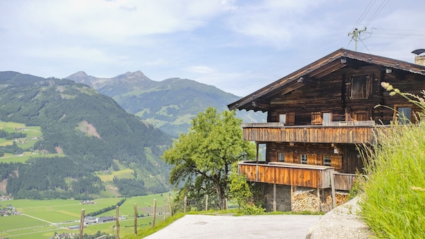 A rustic wooden chalet with a balcony, set against a mountainous backdrop.