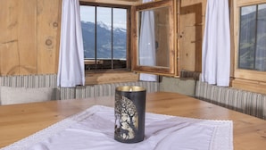 A wooden room with a large window, a wooden table with a candle, and a mirror on the wall.