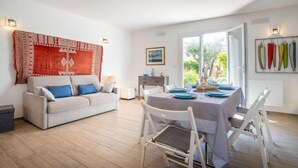 Ein modernes Wohnzimmer mit einer Couch, einem Esstisch und Stühlen. Ein großes Fenster bietet Blick auf grüne Natur.