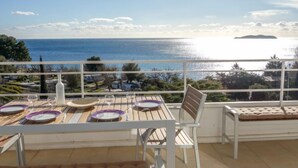 Varanda com mesa posta para dois, com vista para a costa, o mar e uma ilha ao longe.