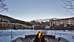 Un foyer en pierre, installé dans une cour, offre une vue sur une chaîne de montagnes et sur des bâtiments en arrière-plan.