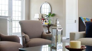 Una sala de estar con un sillón color beige, una mesa de centro de vidrio y una mesita con una vela y objetos decorativos.