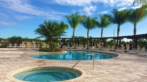 Una piscina con hidromasaje, rodeada de sillas de descanso y palmeras.