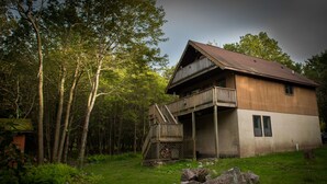 Een houten vakantiehuis met twee verdiepingen en een balkon, omgeven door bomen en een gazon.