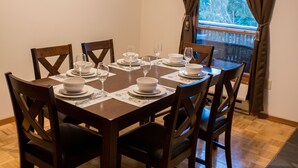 Een eetkamer met een houten tafel voor zes personen, een plafondventilator, een klok en een raam met gordijnen.
