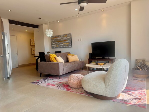 A modern living room with a sofa, a round coffee table, a television, and a ceiling fan.