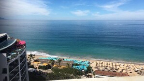 A beachfront hotel with a pool, beach umbrellas, and a view of the ocean.